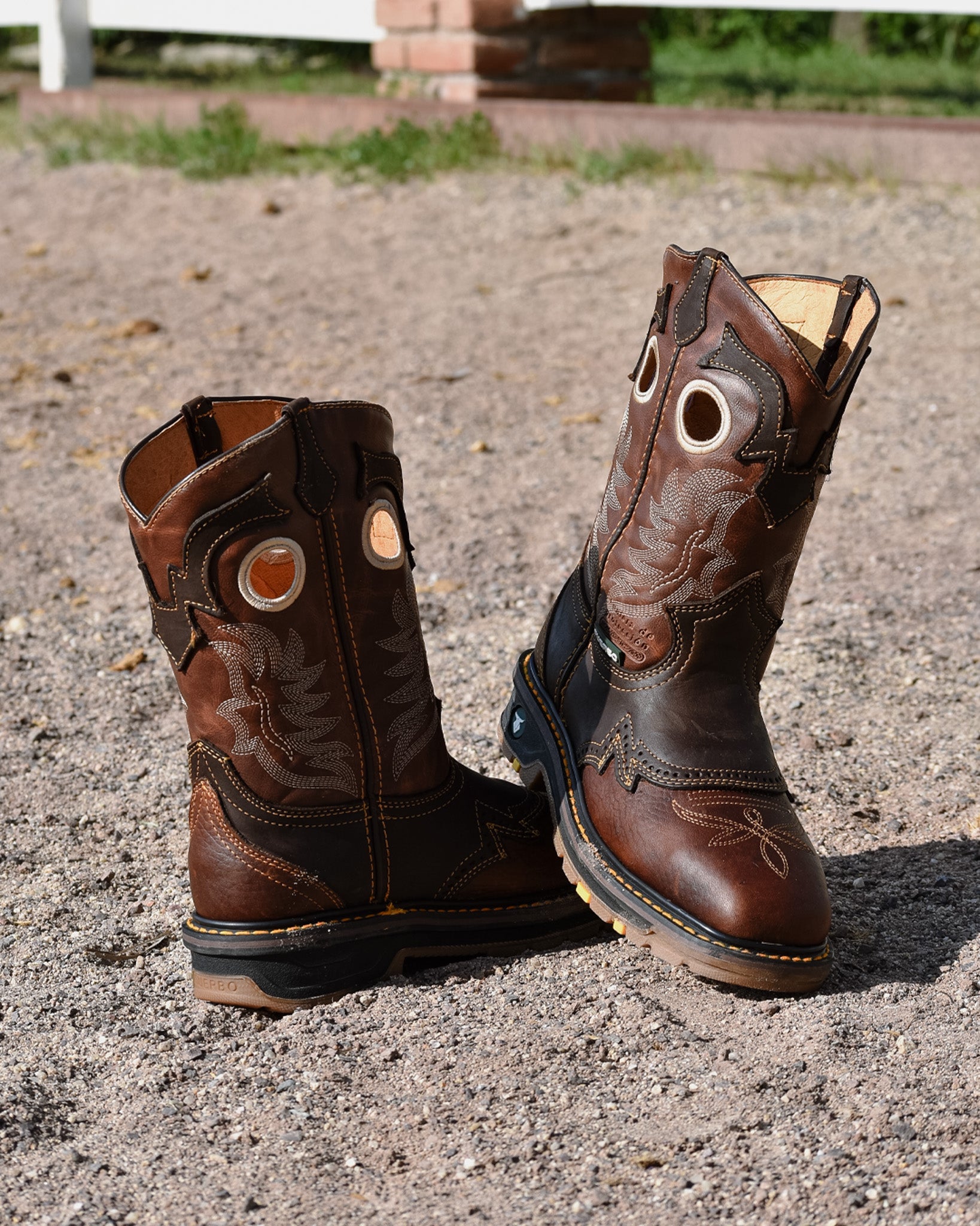 Pair of brown Fuerbo 5038 square-toe rodeo work boots on gravel, showing the stitched shafts and front and rear construction.