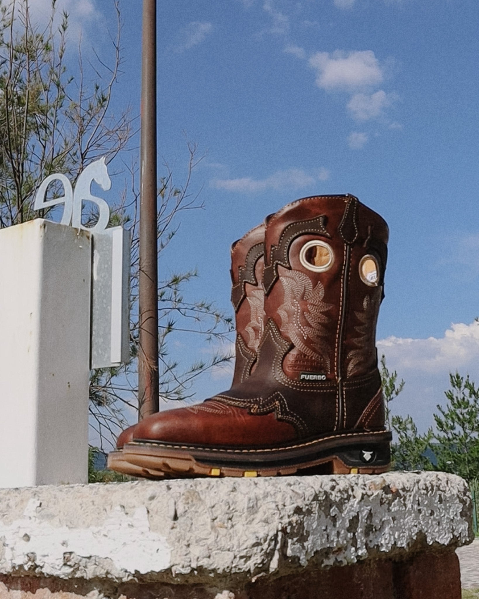 Brown Fuerbo 5038 square-toe rodeo work boot displayed on a concrete ledge beneath a blue sky.